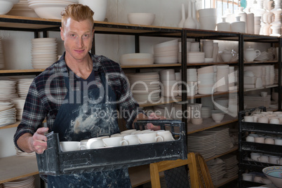 Male potter holding tray of earthenware equipments