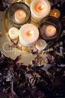 Lit candles and dry leaves on table