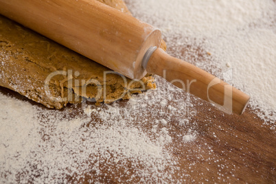 Flattening dough with rolling pin with sprinkled over flour on a wooden table