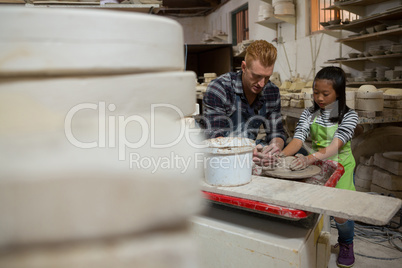 Male potter assisting his daughter in making a pot