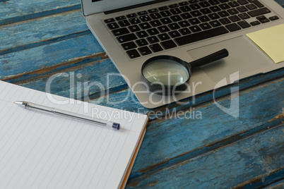 Blank book, magnifying glass and laptop on wooden plank