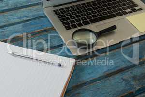 Blank book, magnifying glass and laptop on wooden plank