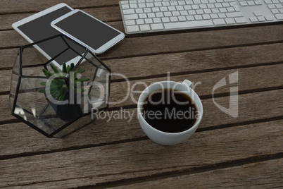 Digital tablet, mobile phone, mouse, pot plant, keyboard and black coffee on wooden plank