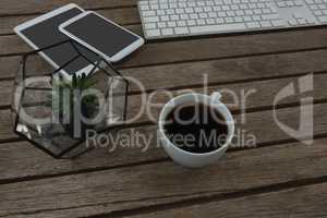 Digital tablet, mobile phone, mouse, pot plant, keyboard and black coffee on wooden plank