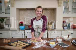 Smiling woman kneading dough in kitchen