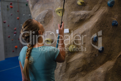 Rear view of athlete standing by climbing wall with rope in fitness studio