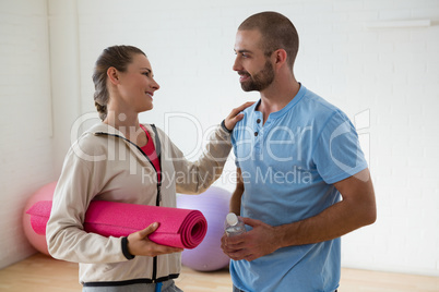 Student holding exercise mat talking to instructor in health club