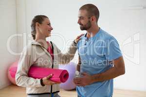 Student holding exercise mat talking to instructor in health club