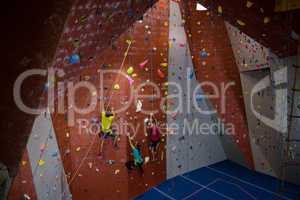 View of trainer and athletes rock climbing in gym