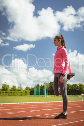 Woman performing stretching exercise on a race track