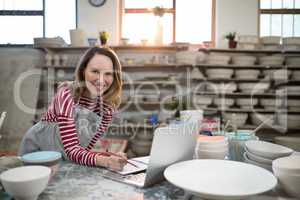 Female potter checking the orders from laptop