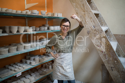 Portrait of female potter standing near shelf