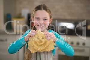 Smiling girl holding dough in kitchen