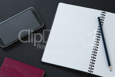 Passport, mobile phone, pencil and organizer on black background