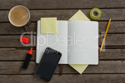 Organizer, coffee, mobile phone and stationery on wooden plank