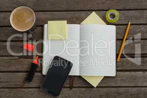 Organizer, coffee, mobile phone and stationery on wooden plank