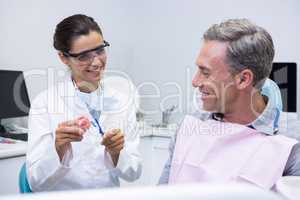Happy dentist teaching man brushing teeth on dental mold