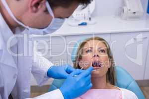 Dentist holding tools while examining woman at medical clinic