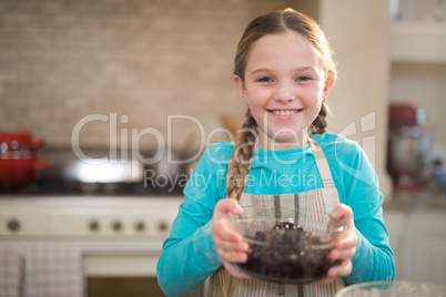 Girl holding bowl of dried blue berries in kitchen