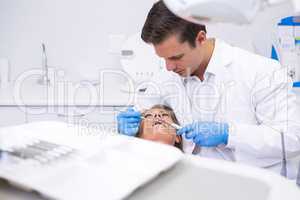 Dentist holding medical equipment while giving treatment to woman
