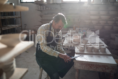 Male potter using digital tablet at worktop