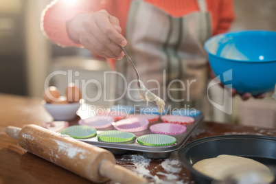 Woman putting muffin batter in paper case in baking tray