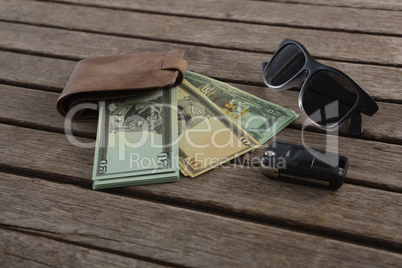 Sunglasses, wallet and currency note on wooden plank