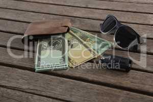 Sunglasses, wallet and currency note on wooden plank