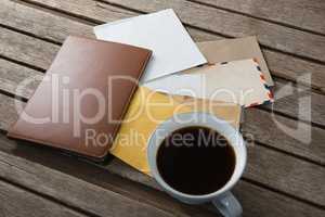 Coffee with various envelopes and diary on wooden plank