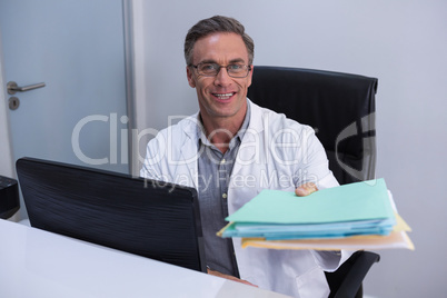 Portrait of dentist holding file while sitting by computer