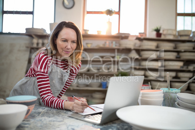 Female potter checking the orders from laptop