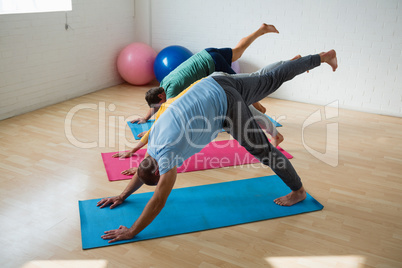 Male instructor with students practicing downward facing dog pose with feet up