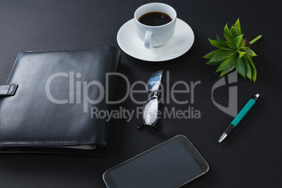 Black coffee, flora, pen, spectacles, mobile phone and organizer on black background