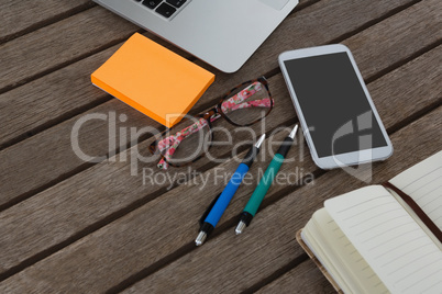 Mobile phone, laptop, pen, sticky note, spectacles and organizer on wooden plank