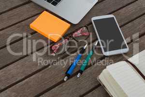 Mobile phone, laptop, pen, sticky note, spectacles and organizer on wooden plank