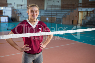 Smiling female volleyball player standing with hand on hips in the court