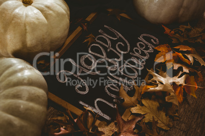 View of happy Halloween text on slate with pumpkins and autumn leaves