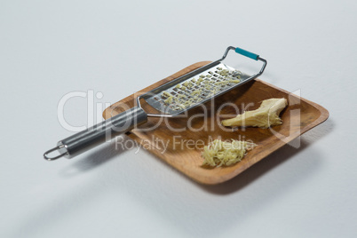 High angle view of steel grater and ginger on wooden plate
