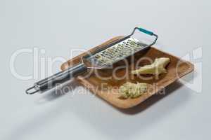 High angle view of steel grater and ginger on wooden plate