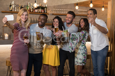 Happy friends taking selfie while having drinks