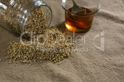 Grains spilling out of jar with bowl of honey