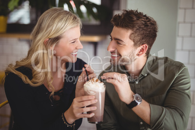 Smiling couple holding fresh dessert in glass at coffee shop