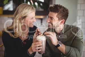 Smiling couple holding fresh dessert in glass at coffee shop