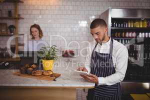 Young waiter using digital tablet while standing by counter