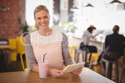 Portrait of smiling young blond woman sitting with tablet and milkshake