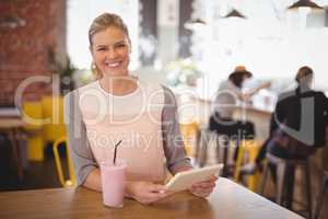 Portrait of smiling young blond woman sitting with tablet and milkshake