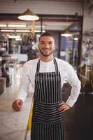Portrait of smiling waiter standing with hand on hip by counter