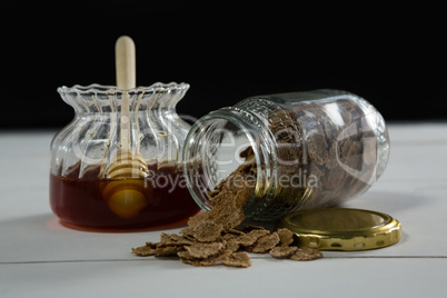 Jar of honey and wheat flakes spilling out of bottle