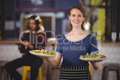Portrait of smiling young waitress standing with fresh salad plates