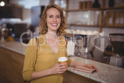 Portrait of smiling young female customer holding disposable coffee cup at counter